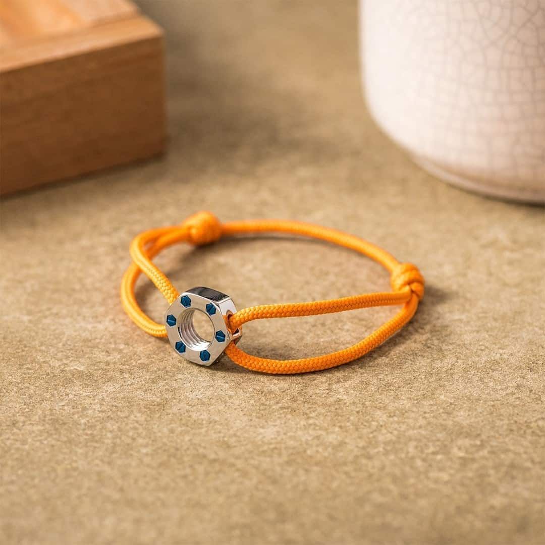 Bracelet cordon orange avec breloque en forme de noix argentée, détails bleus, sur une surface beige.