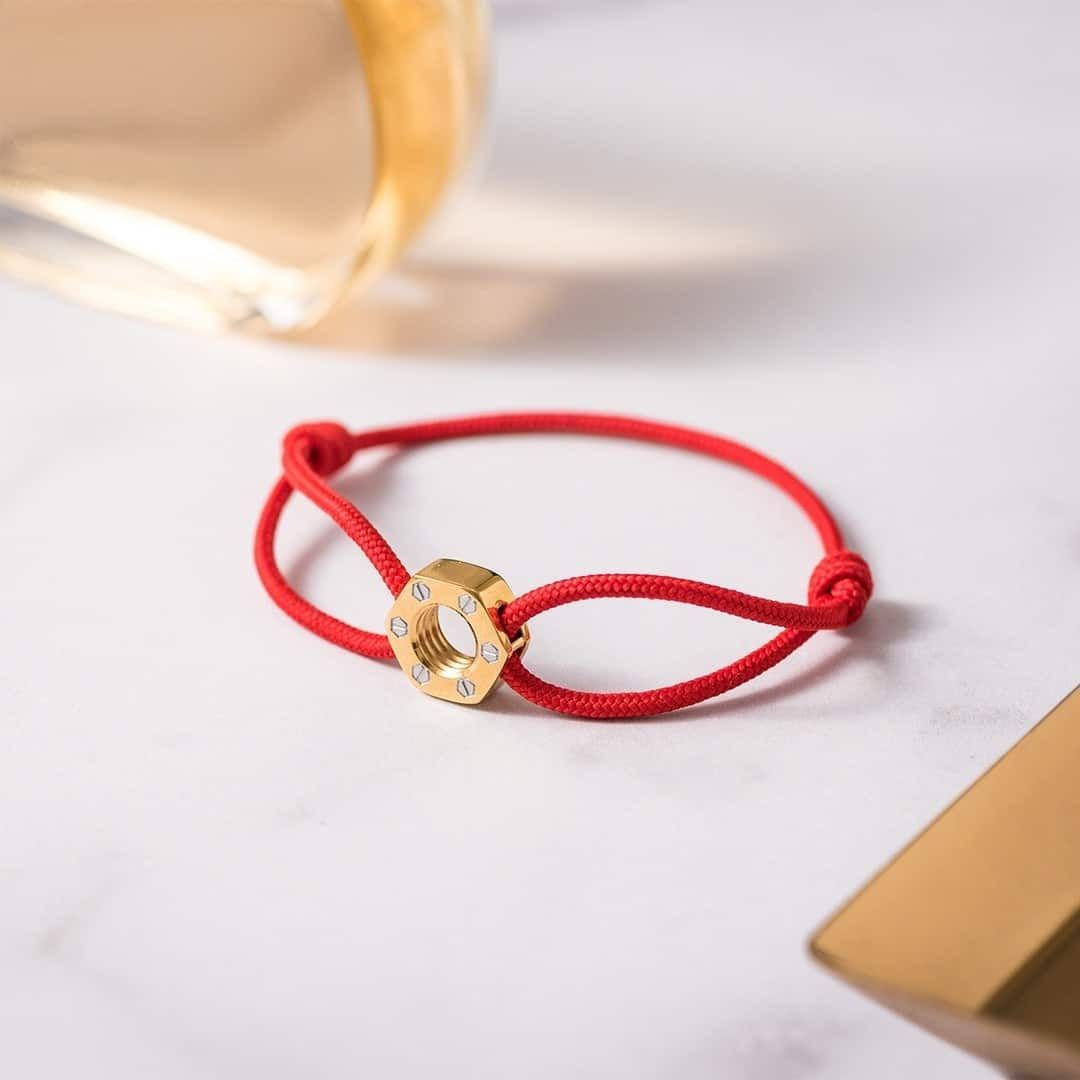 Bracelet cordon rouge avec anneau en or, diamants, reposant sur une surface en marbre, avec un fond flou.