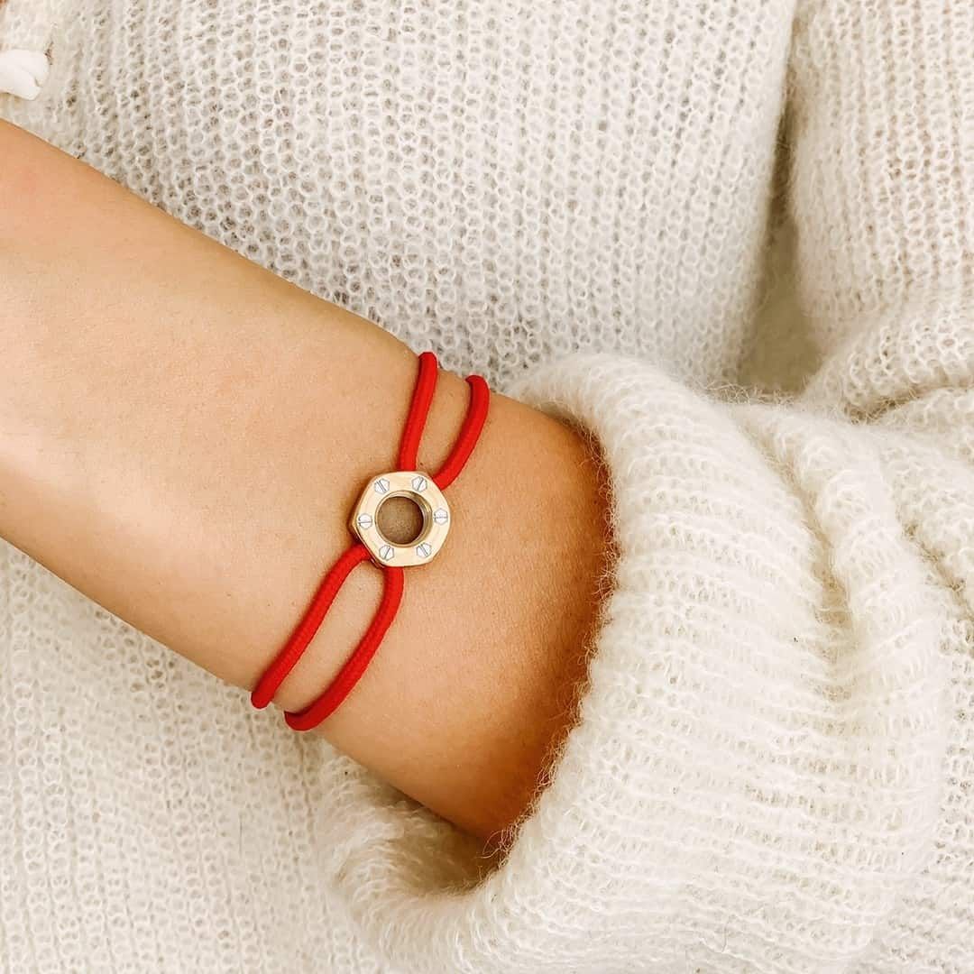 Personne portant un bracelet en fil rouge avec une breloque circulaire de couleur dorée ; le bras est contre un pull blanc.