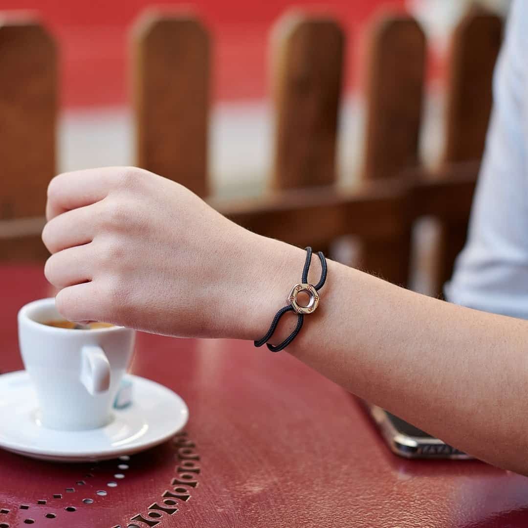 Poignet d'une femme avec un bracelet sombre près d'une tasse à café sur une table rouge.