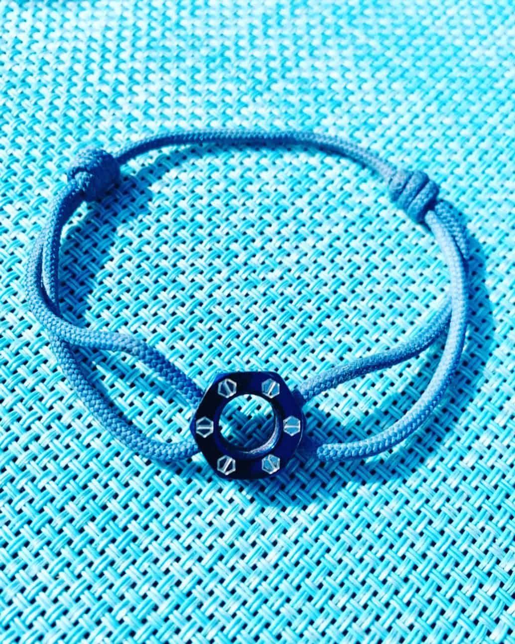 Bracelet bleu avec une pièce centrale foncée ornée de cristaux, sur un fond tissé turquoise.