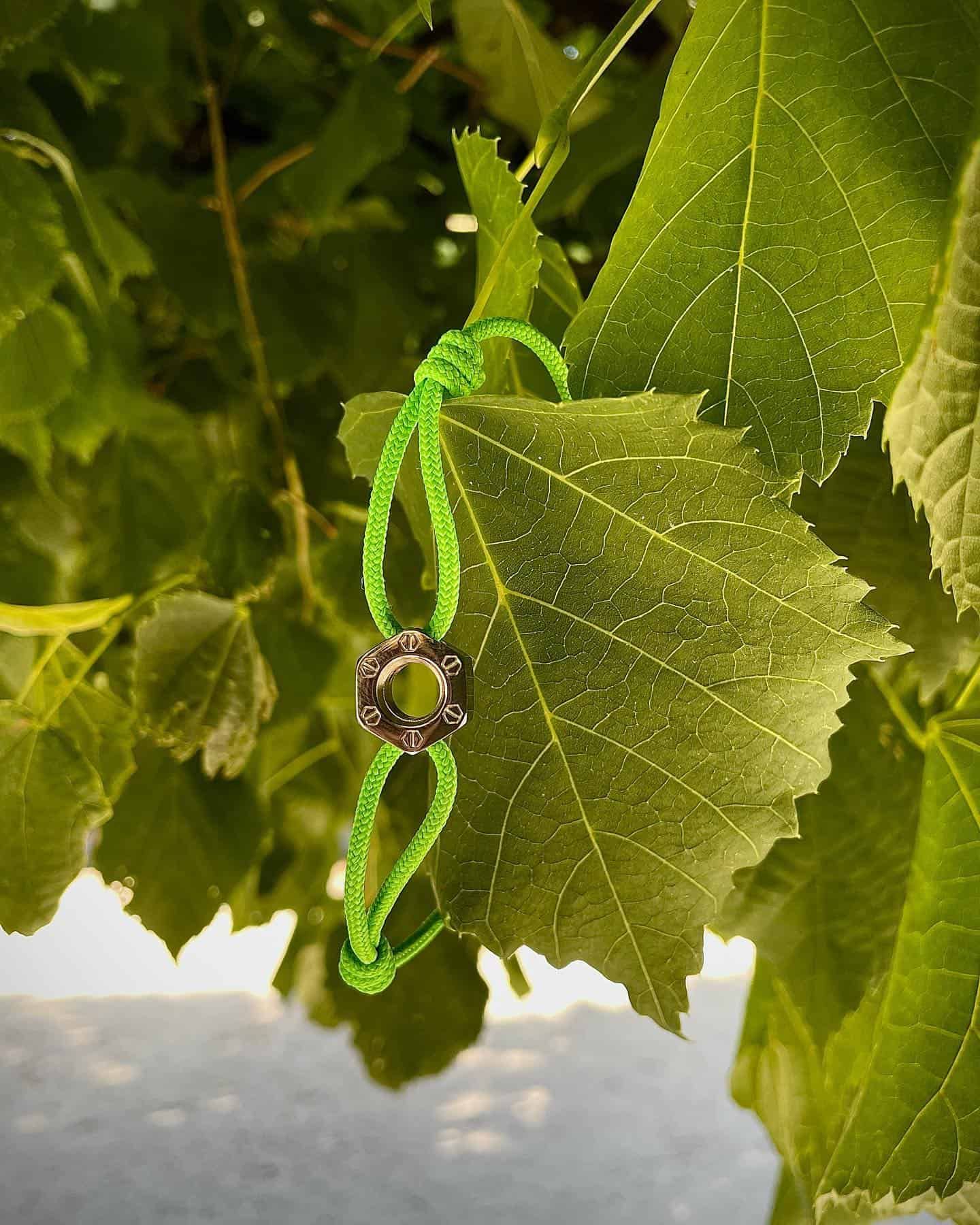 Bracelet vert avec une pièce maîtresse sombre suspendue à une feuille verte dans un arbre.