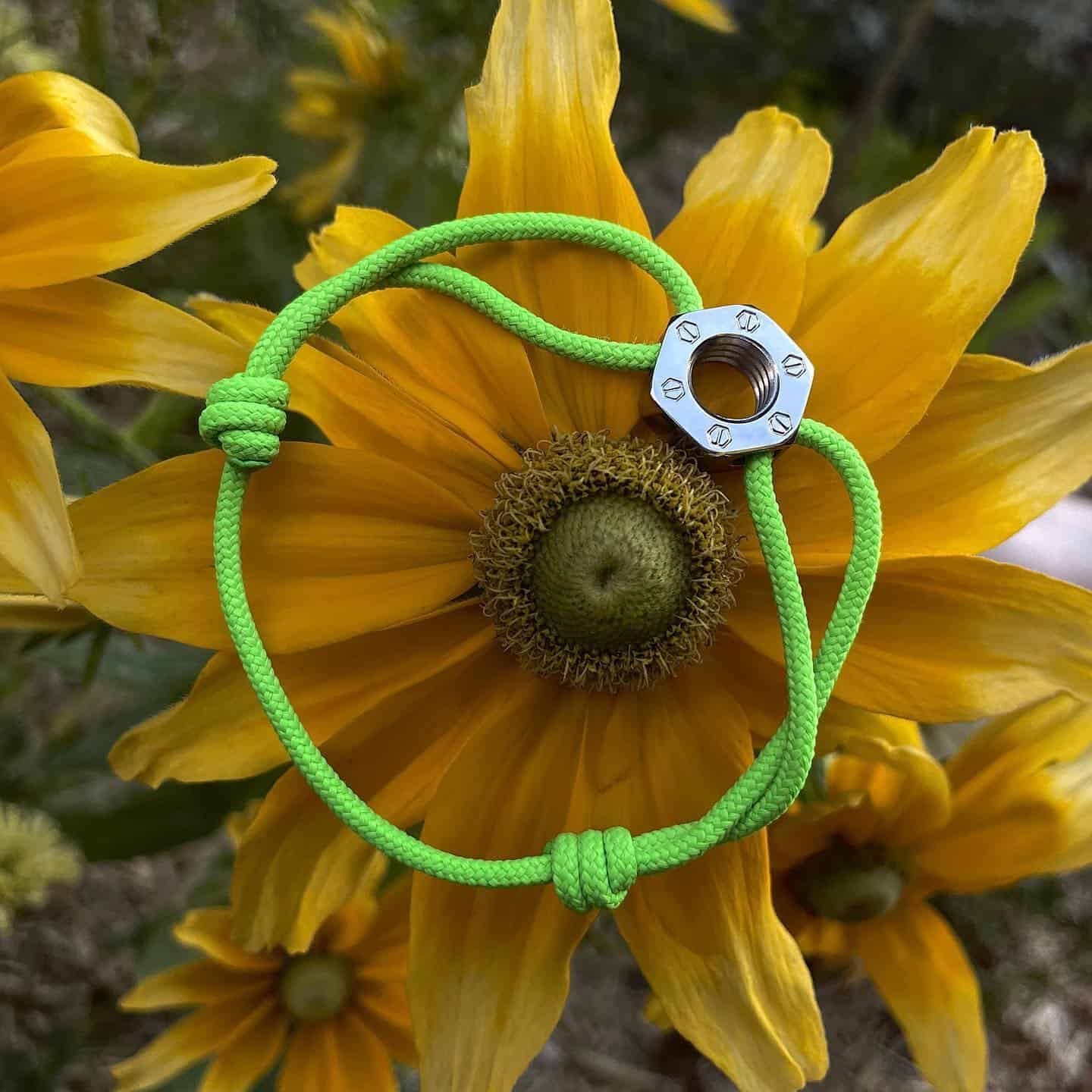 Bracelet en corde verte avec un accent métallique sur une fleur jaune.