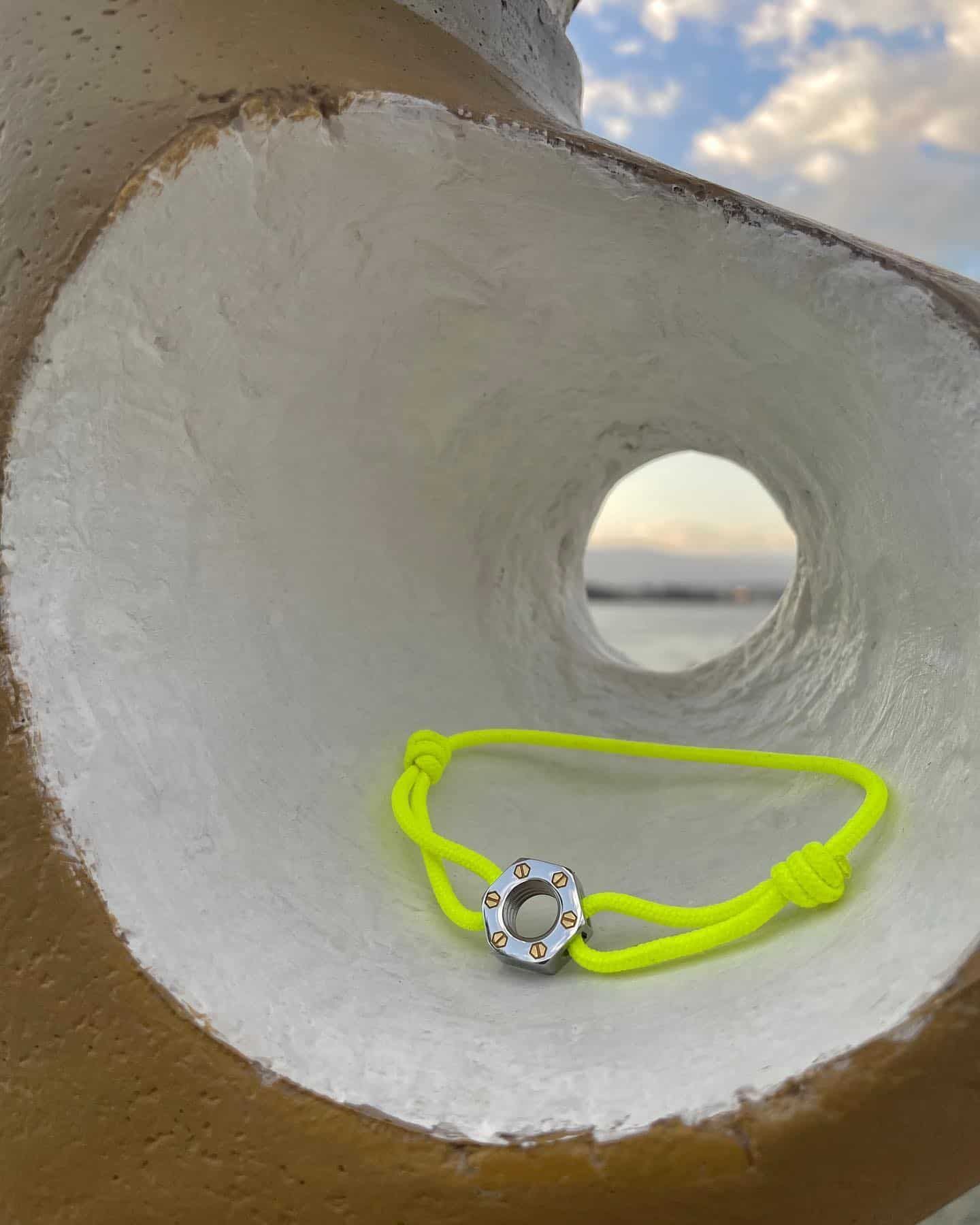 Un bracelet jaune fluo avec un fermoir en argent se trouve dans un trou blanc surplombant l'océan.