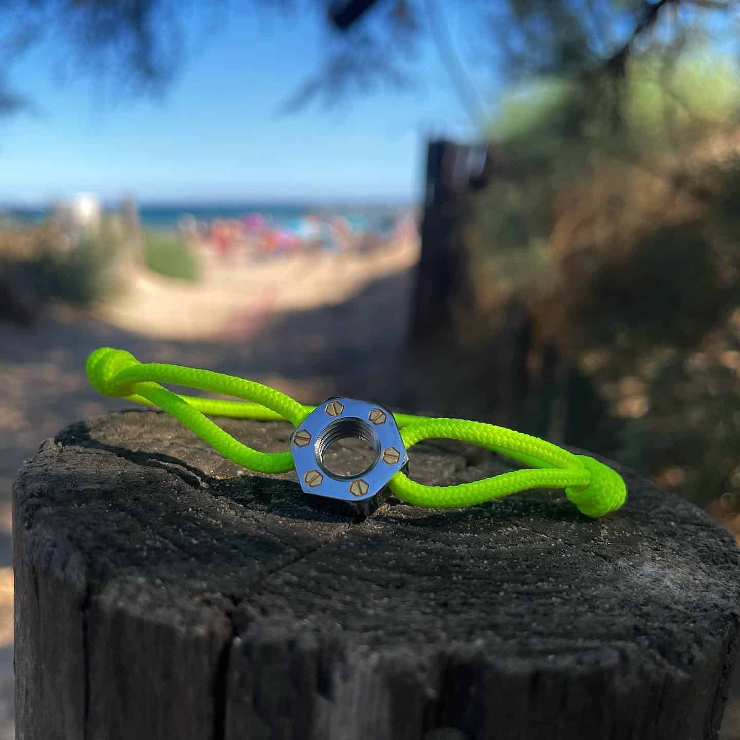 Bracelet vert fluo avec centre argenté sur un poteau en bois, scène de plage en arrière-plan.
