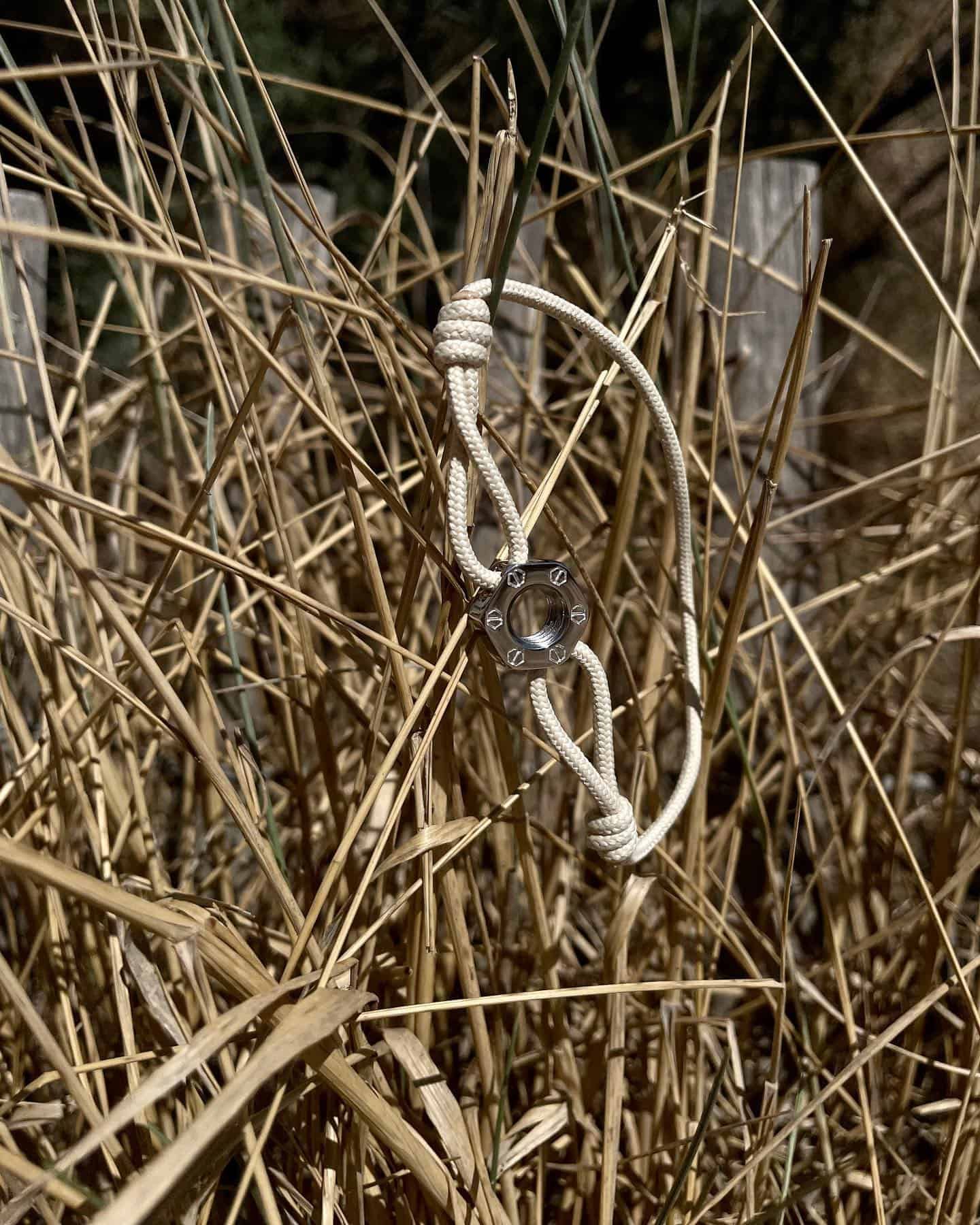 Une corde blanche avec un pendentif en argent emmêlé dans de l'herbe brune sèche.