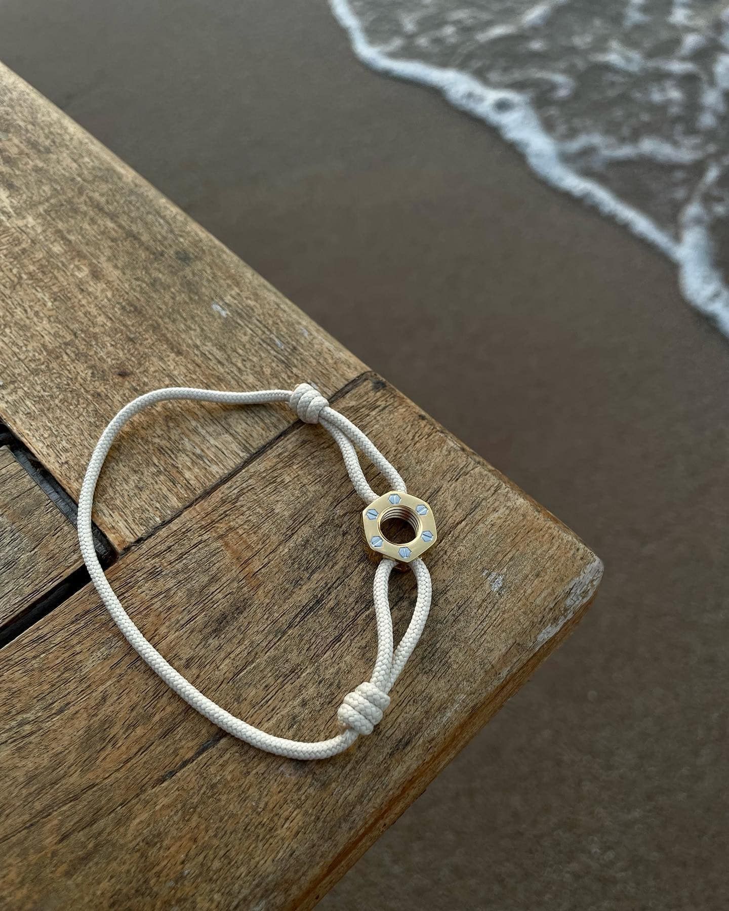 Bracelet blanc avec breloque en forme de cercle doré sur une surface en bois près de l'océan.