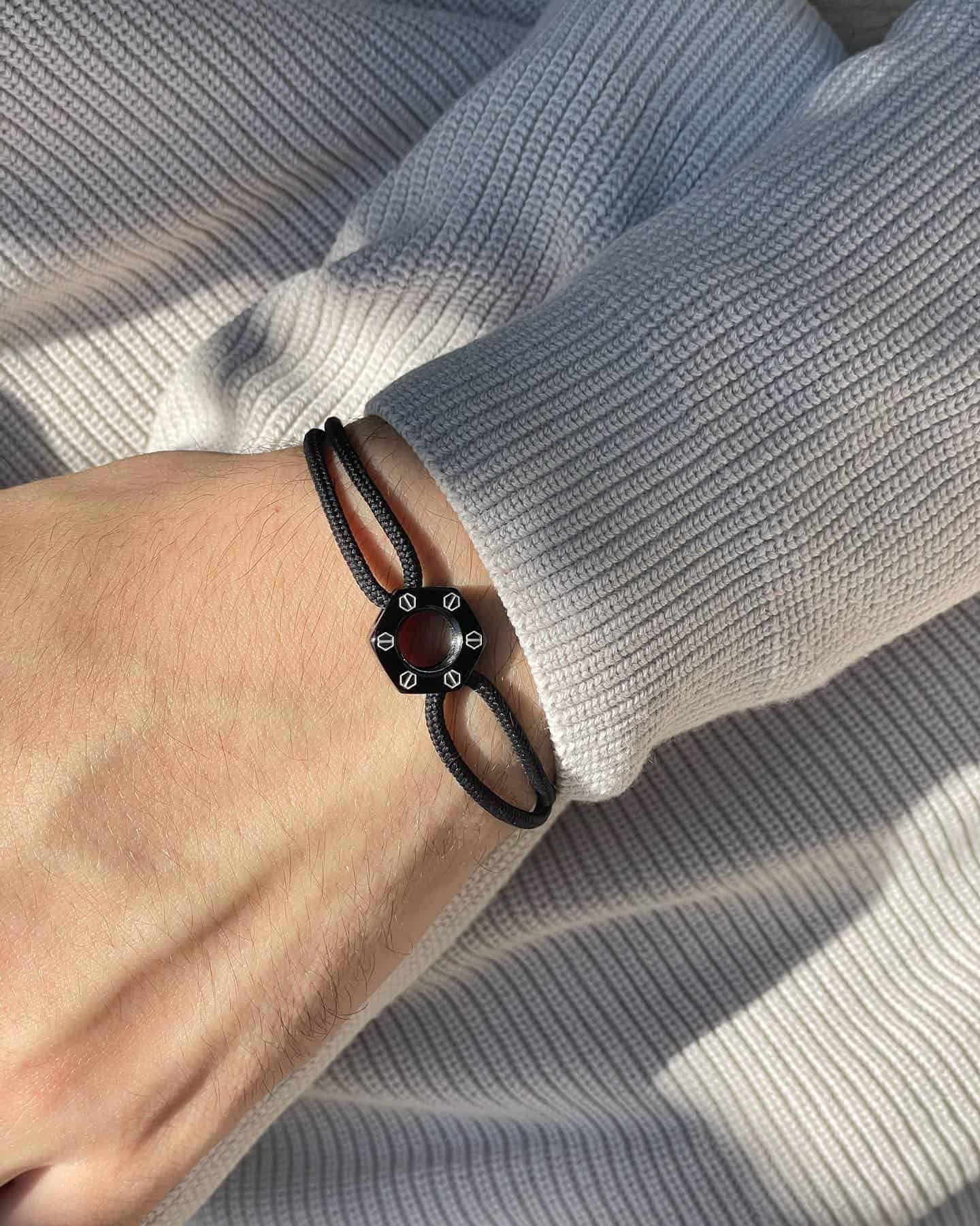 Bracelet noir avec une pierre centrale foncée sur un poignet, sur un pull blanc.
