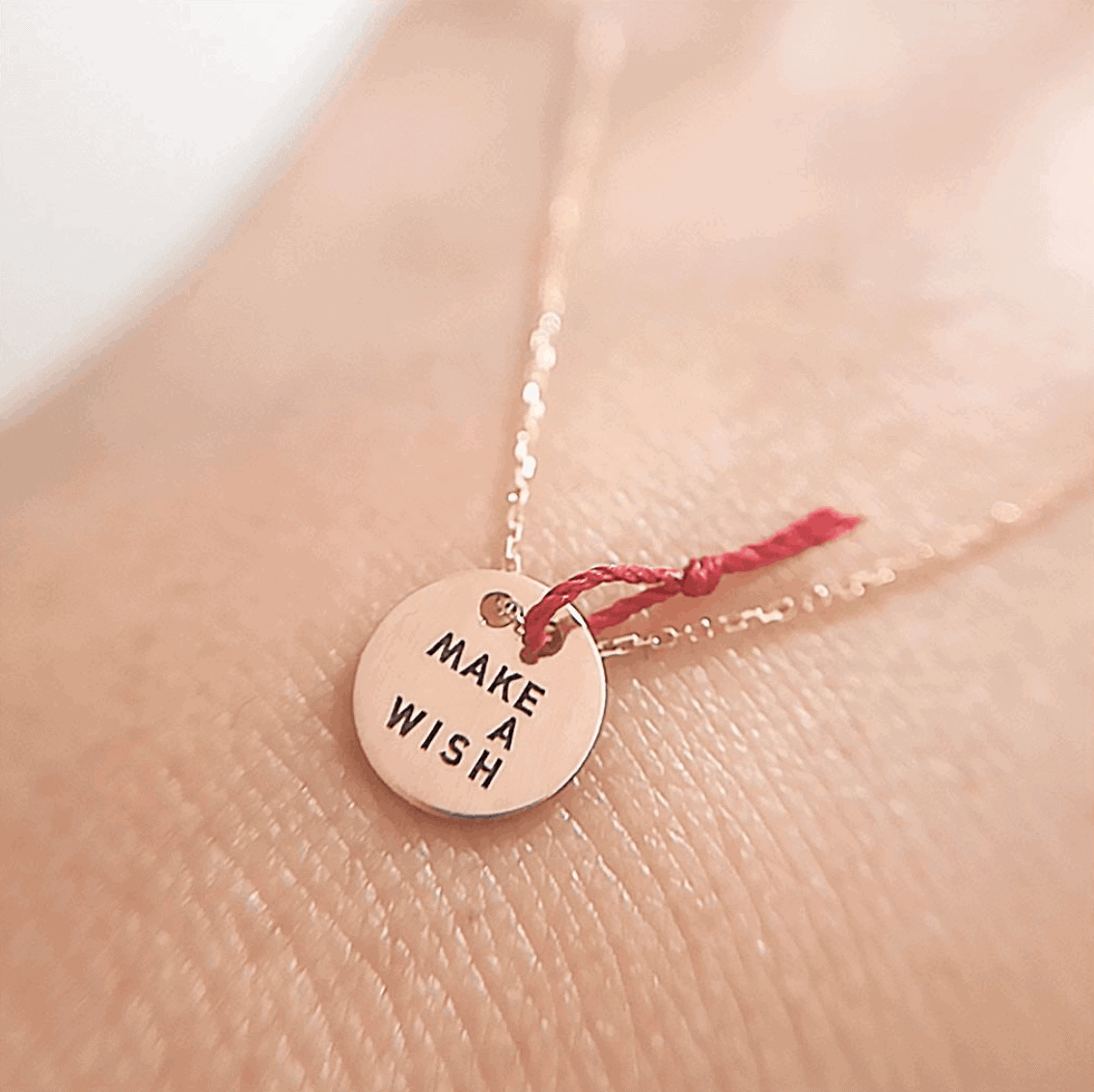 Un collier en or rose sur un poignet a un pendentif en forme de disque avec