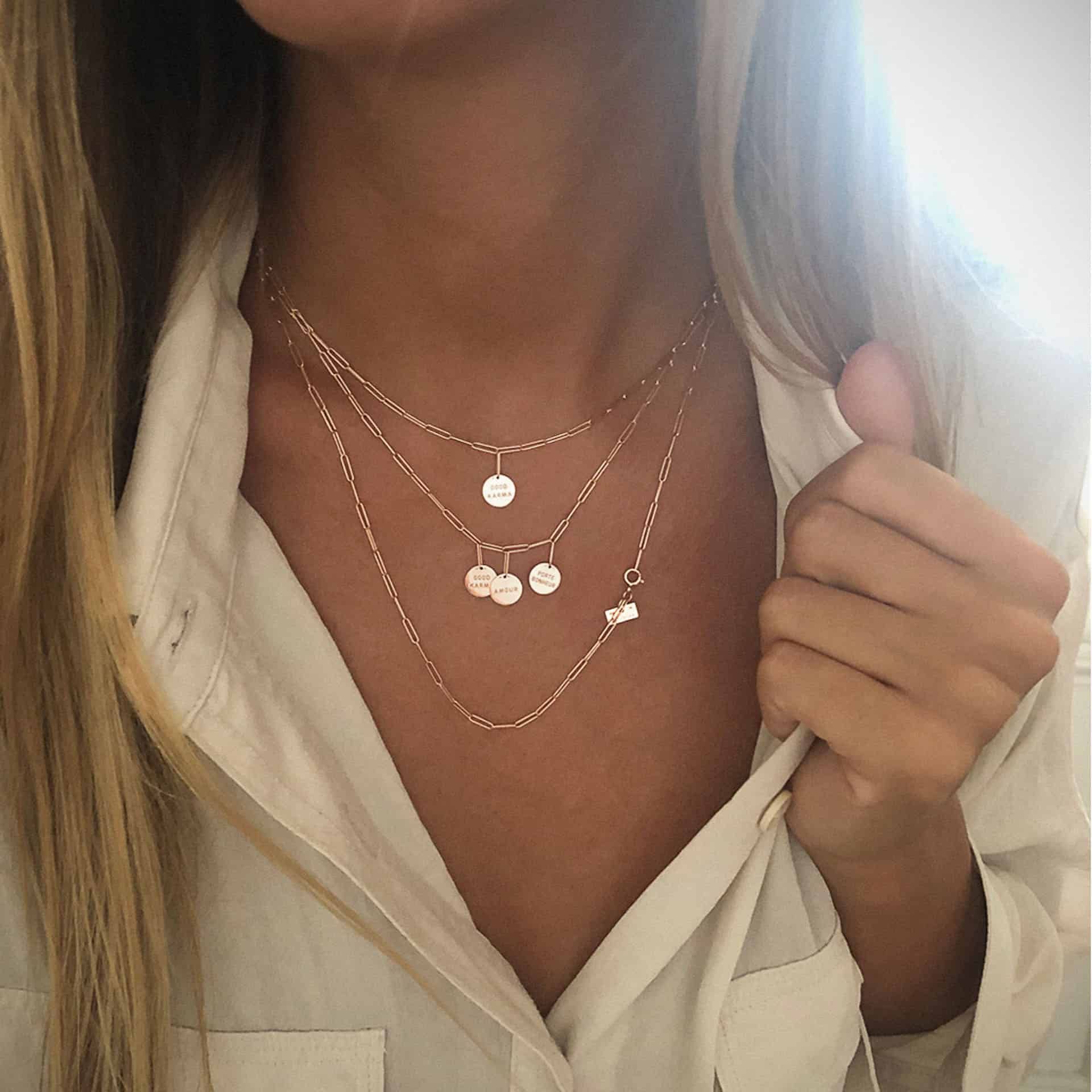Femme portant des colliers à plusieurs couches avec des détails de pendentif, vêtue d'une chemise blanche.