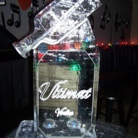 Clear glass trophy with “Ultima” script on a dark nightclub table, surrounded by colorful lights