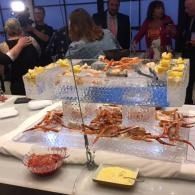 Seafood buffet table with crab legs, shrimp, and dips, with people mingling in the background