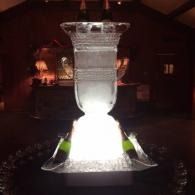 Illuminated white glass vase ice sculpture centered in a dark room, glowing against a black background