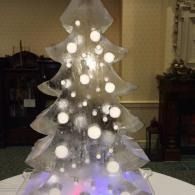 White, illuminated ice sculptured Christmas tree with glowing ornaments in a dim room