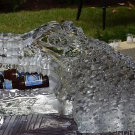 Clear ice sculpture with a bottle embedded inside, outdoors on a table