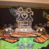 Buffet table with trays of food in front of a black-and-green backdrop at an event