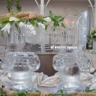 Clear ice sculptured welcome sign with floral greenery and two transparent pedestal stands