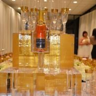 Ice sculpture with a champagne bottle on a banquet table, with glass towers and guests in the background