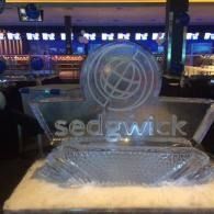 Sedgwick ice sculpture on a bar counter with blue-lit background and blurred bottles