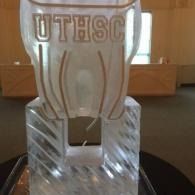Clear trophy with etched letters, displayed on a dark round table indoors.