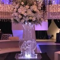 Glass vase with white floral centerpiece and glowing “49” table number at a decorated event venue