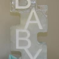 Vertical white letters B, A, B, and Y on a clear hanging ornament against a beige background
