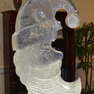 Clear ice sculpture of a crescent moon shaped Santa head with a dark background and plant behind it