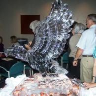 Large reflective sculpture at a crowded indoor event, with people standing around it
