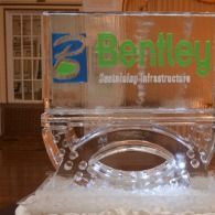 Clear acrylic Bentley logo plaque with green text on a wooden background