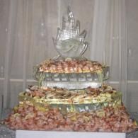 Tiered ice sculptured food display with shrimp on the layers on a table with draped curtains behind.