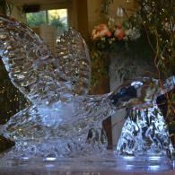 Glass bird ice sculpture with outstretched wings on a table, reflecting light indoors