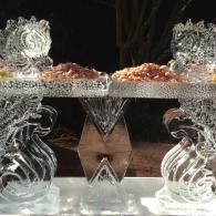 Ice sculptured serving table with mirrored décor, glass candle holders, and bowls of snacks on a silver surface
