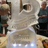 Anniversary display with glowing “Town Village” sign and two people standing beside it