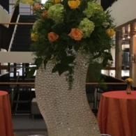 Tall white floral arrangement with orange roses in a lobby dining area