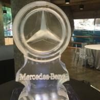 Mercedes-Benz logo ice sculptured display in a dim indoor showroom with a glowing clear acrylic stand