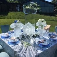 Blue and white outdoor table setting with flowers and glass centerpieces on a patio table