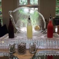 Decorative drink station with red, yellow, and dark bottles on an ice-laden tray and glassware