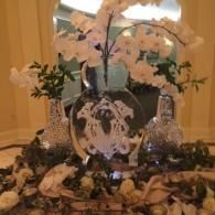 Decorative floral centerpiece with white orchids, candles, and silver accents on a banquet table