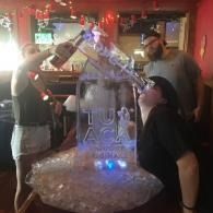 Two people beside an ice sculpture with blue lights in a dimly lit bar