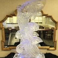 Abstract clear glass-like ice sculpture in front of a gold-framed mirror reflecting a dining room