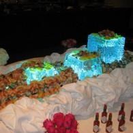 Food display ice sculpture with 3 cubed blue light inside blocks with seafood on top and around.