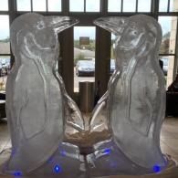 Two translucent penguin ice sculptures facing each other indoors, with blue lights at the base.
