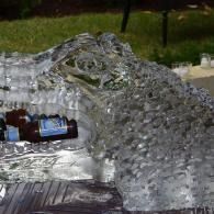 Clear ice sculpture with drink bottles arranged inside, displayed outdoors at night.