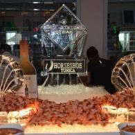 Seafood display with an ice sculpture at a formal event, lit with warm orange lights and shrimp