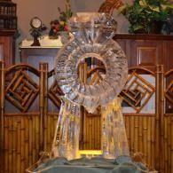 Clear crystal ring sculpture on a stage with bamboo backdrop and flowers, lit warmly