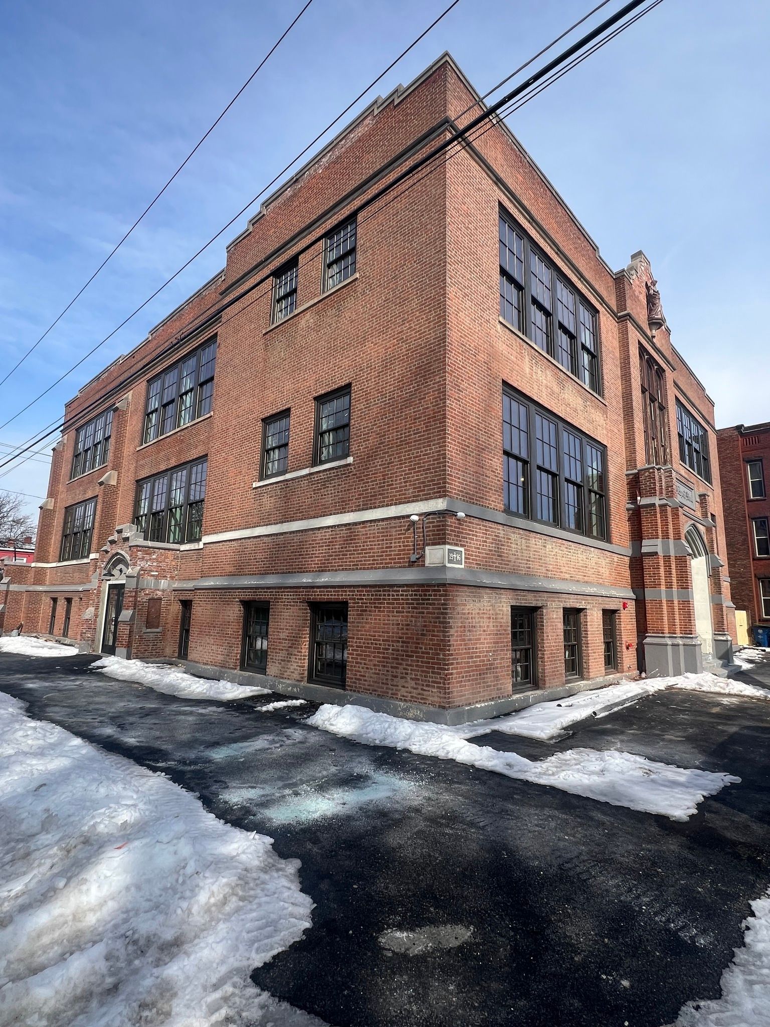 Brick building with snow, asphalt, and power lines.