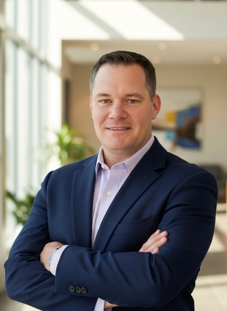 Man in blue suit, arms crossed, smiling. Natural light, office setting.