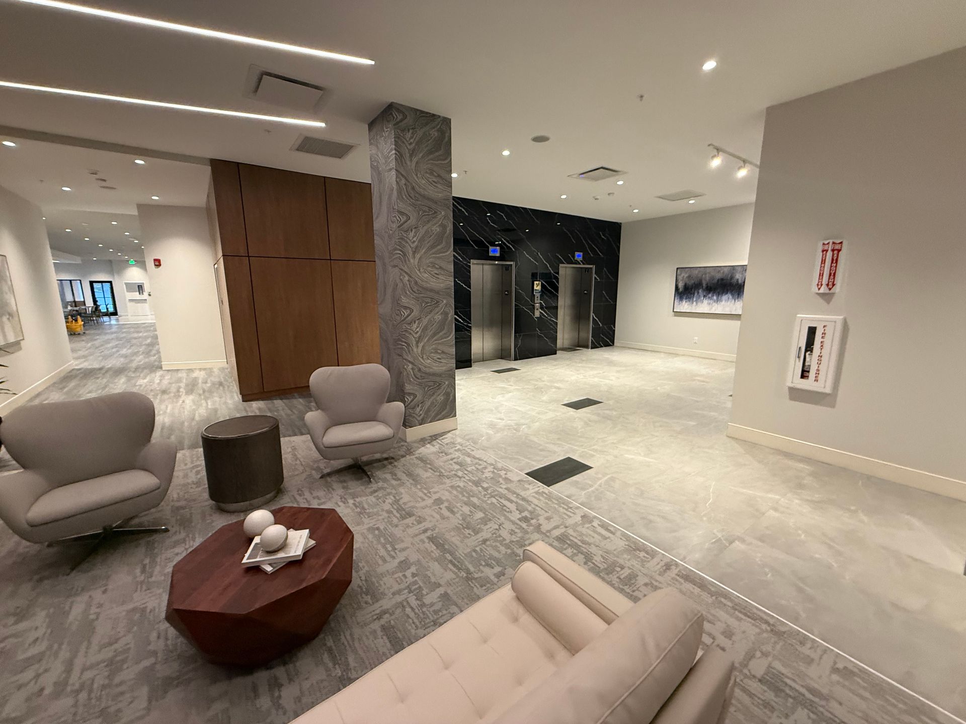 Lobby with seating, elevators, art, and a fire extinguisher. Neutral colors and modern design.