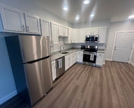 Bathroom with a white vanity, gray countertop, and gray wood-look flooring. White tub/shower combo.