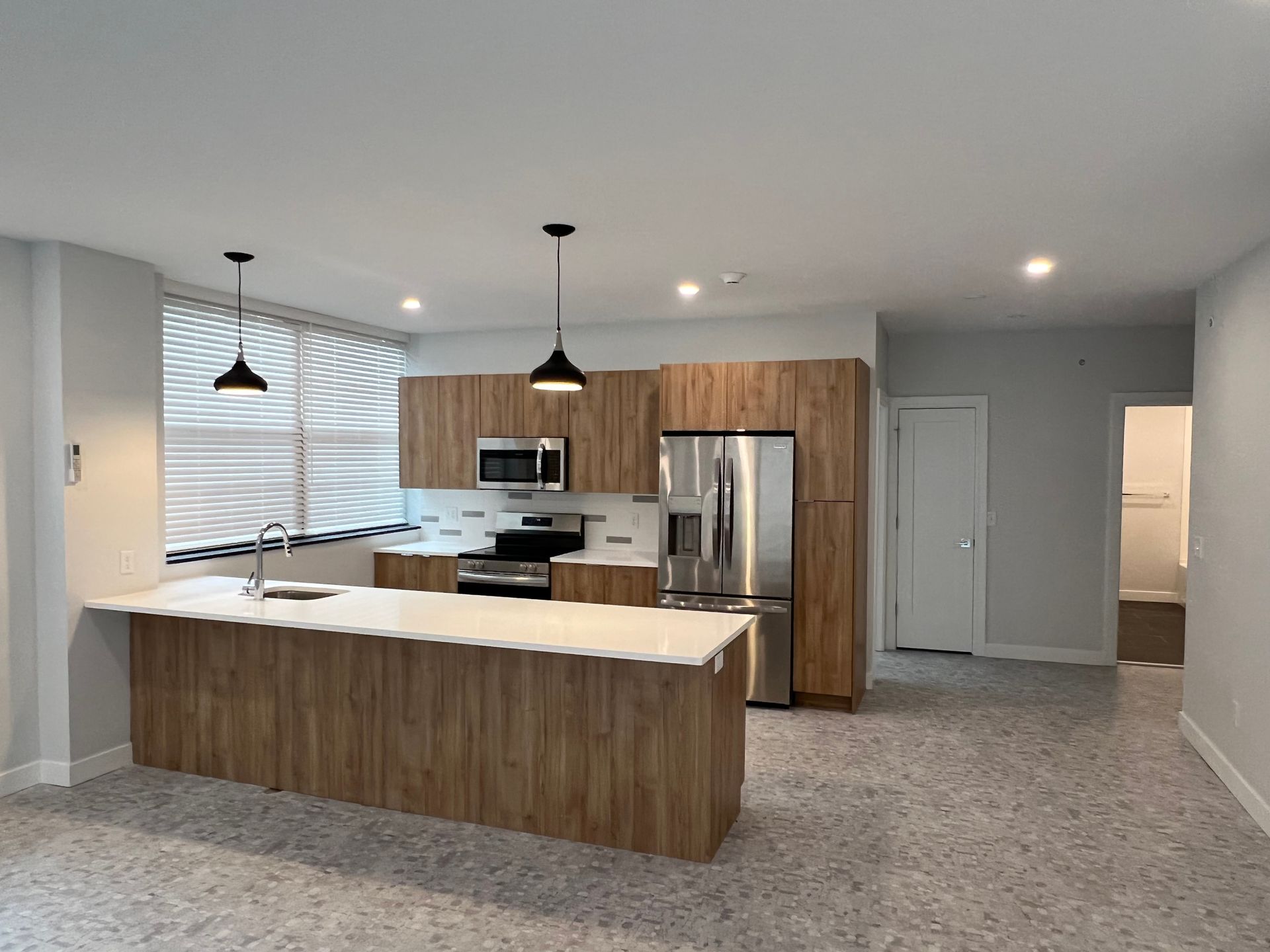Modern kitchen with wood cabinets, island, stainless steel appliances, and terrazzo flooring.